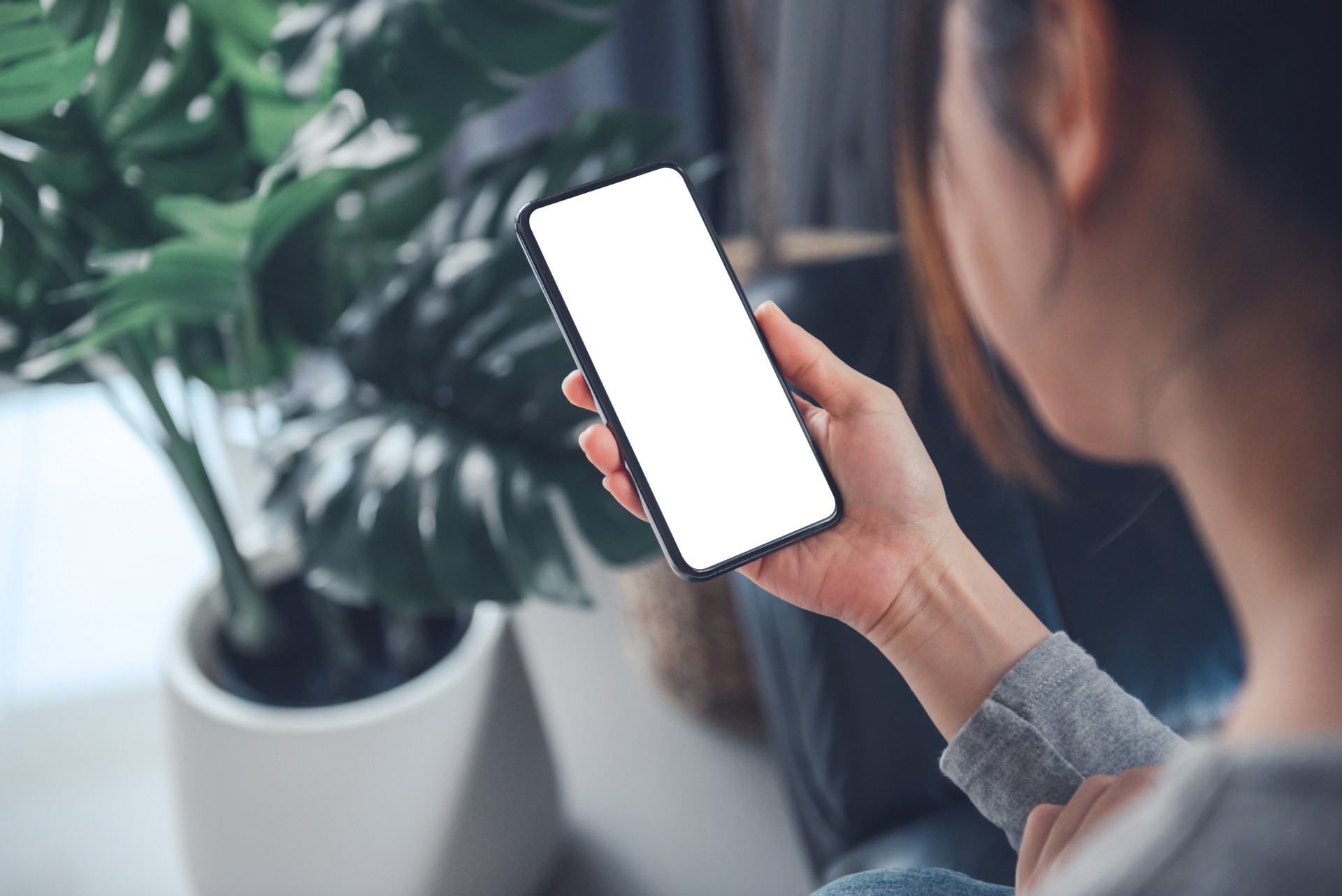 Smartphone mockup. Women hand using mobile phone on sofa at home office. White screen empty space for design concept.